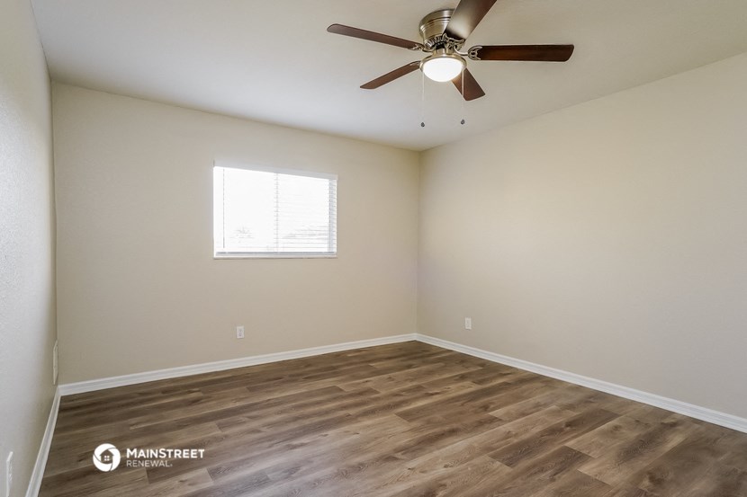 the spacious living room with wood flooring and a ceiling fan