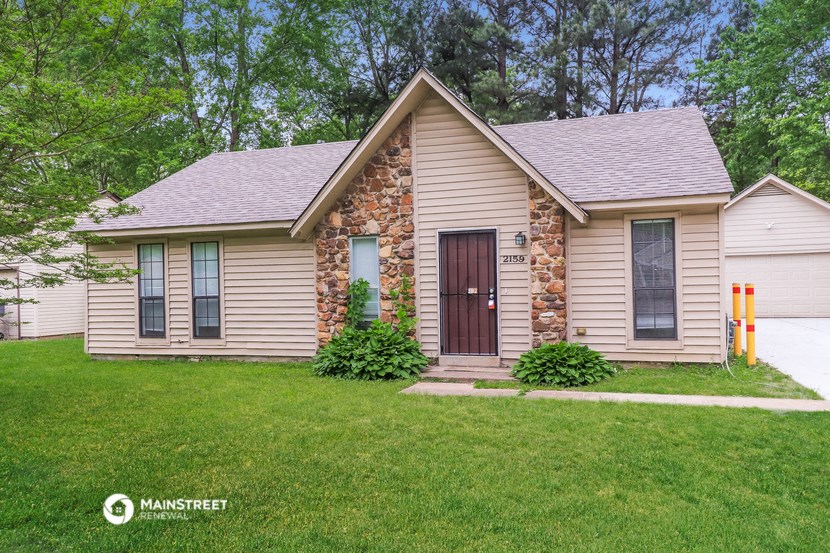 the front of a tan house with a brown door and green grass