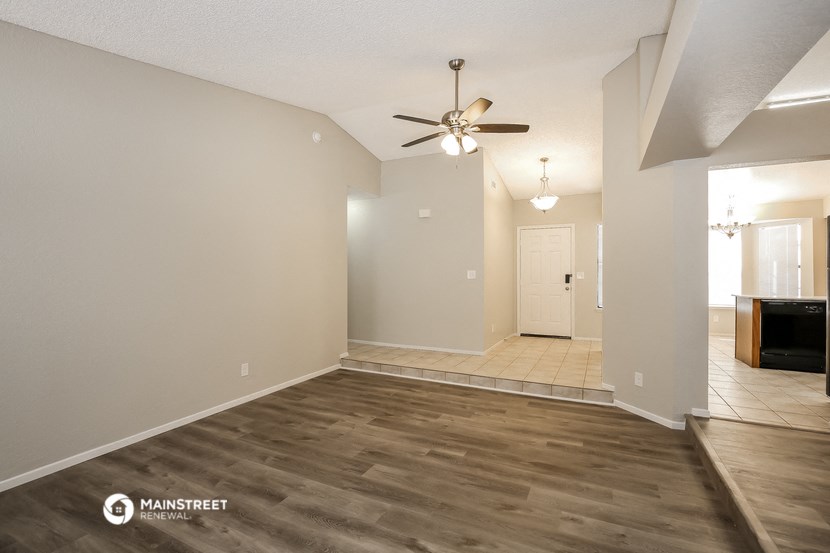 a spacious living room with a ceiling fan and white walls
