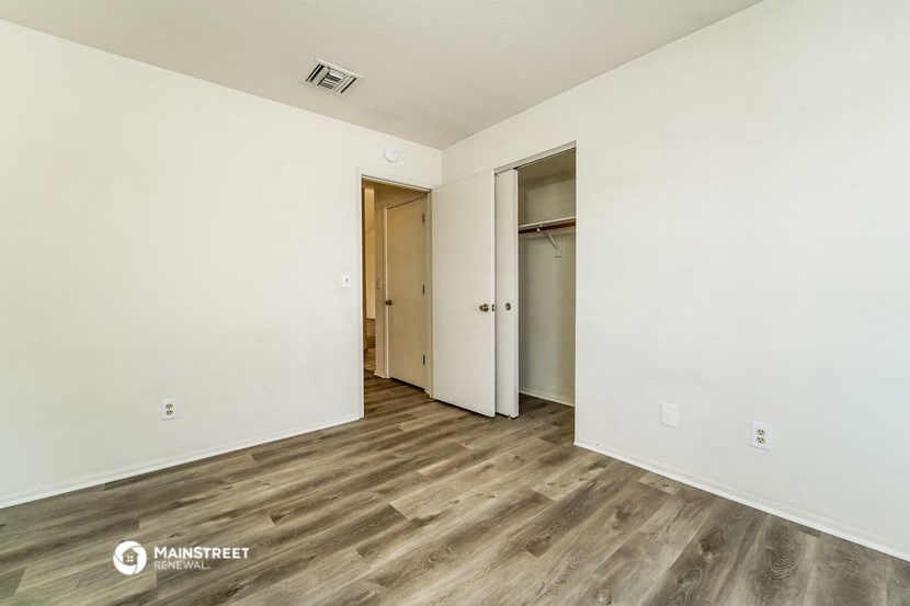the living room of an apartment with white walls and wood flooring