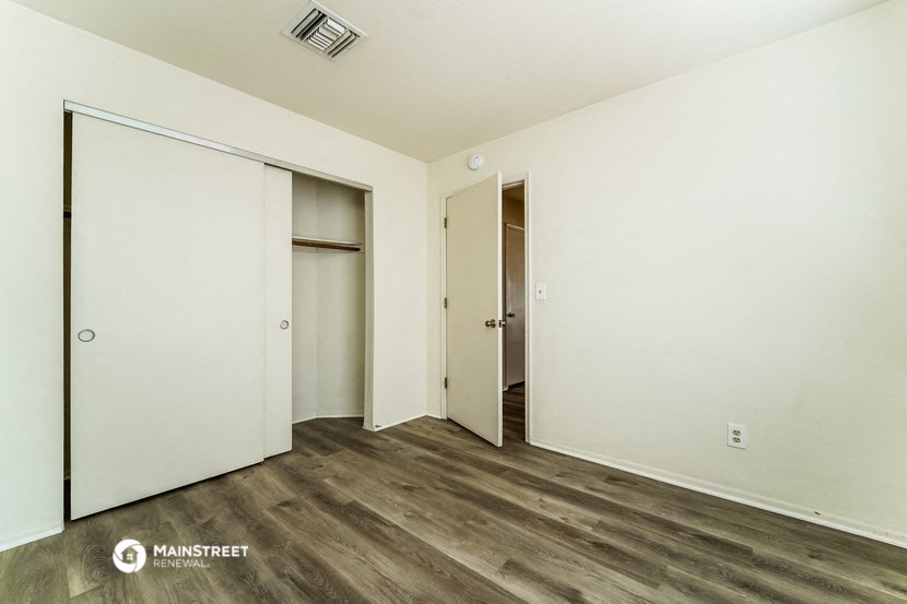 a bedroom with white walls and wood flooring and a closet