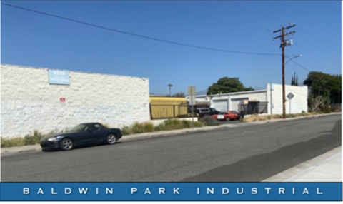 A car is driving on a road past a white wall with a sign that says Baldwin Park Industrial.