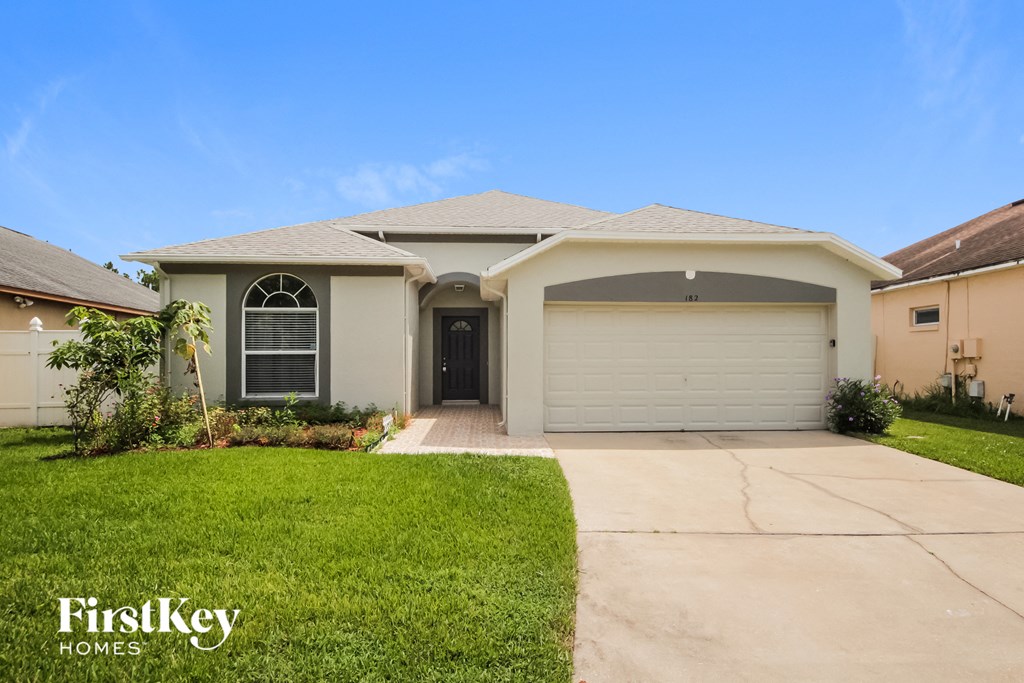a beige house with a garage door and a lawn