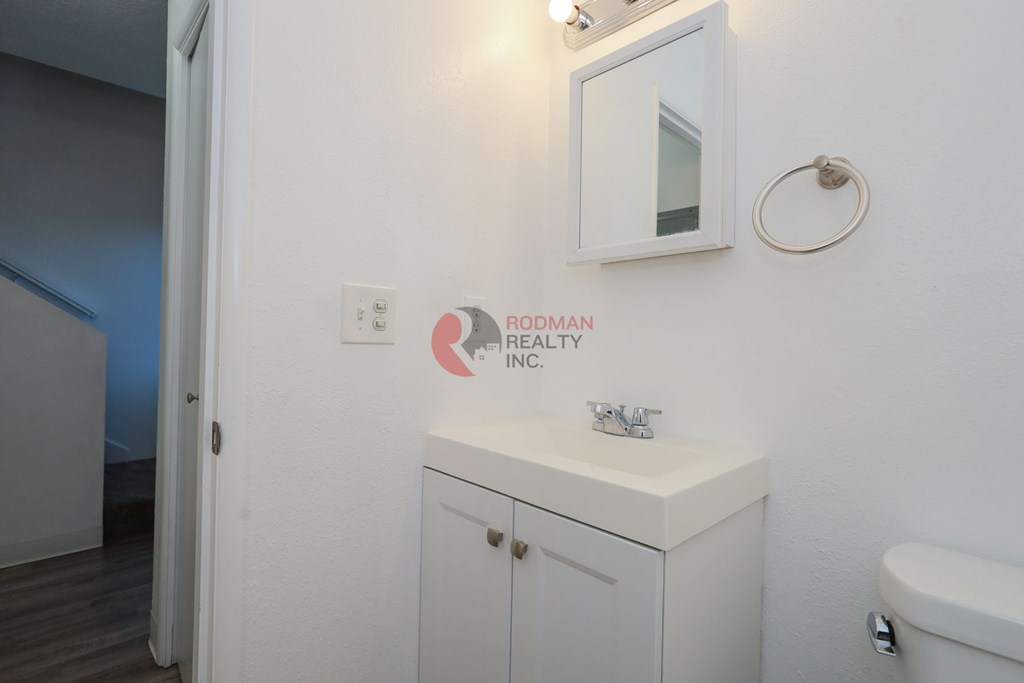 A bathroom with a toilet, sink, and a mirror on the wall.