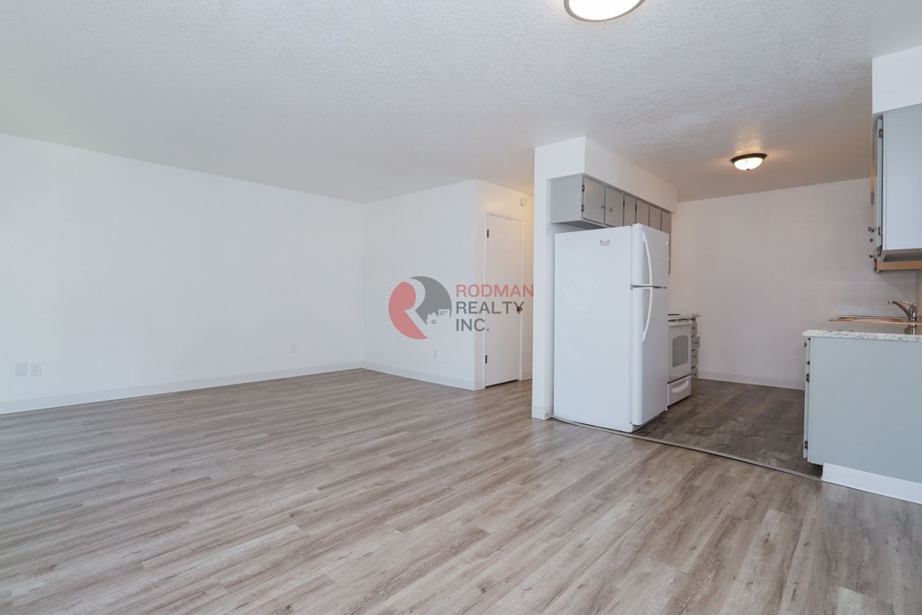 A room with a white refrigerator and wooden flooring.