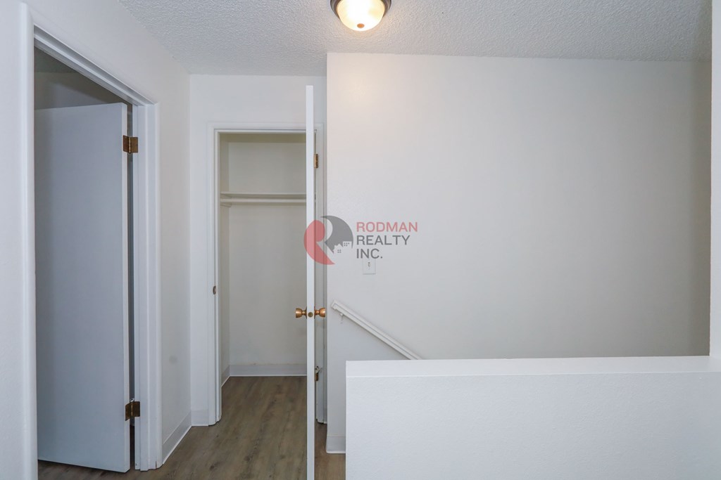 A white hallway with a door on the left and a staircase on the right.