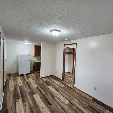 A room with wooden flooring and a white refrigerator.