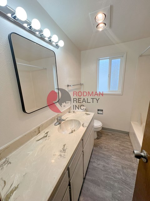 A bathroom with a mirror, sink, toilet, and a window.
