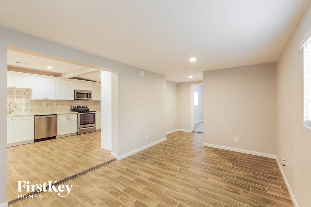 A spacious room with wooden flooring and a kitchen area in the background.