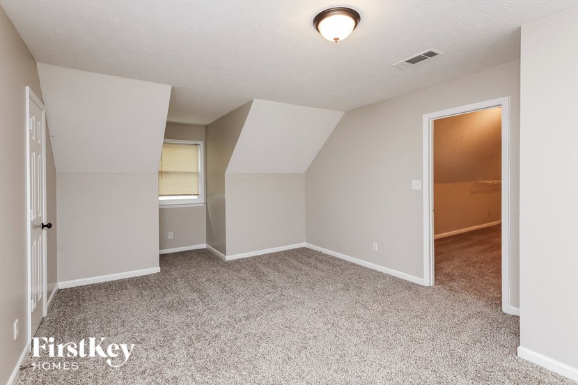 a bedroom with white walls and carpet and a door to a closet