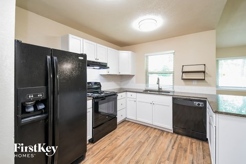 A black fridge in a kitchen with wooden floors and white cabinets.