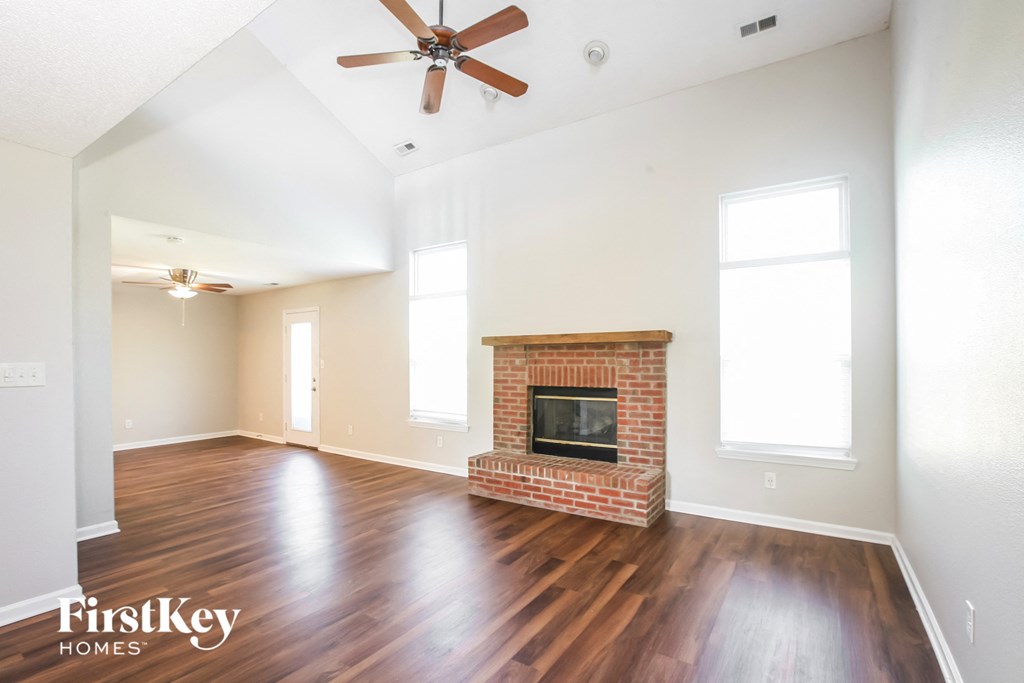 an empty living room with a brick fireplace and wooden floors