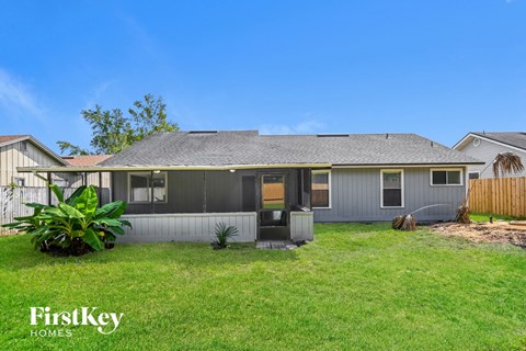a small gray house with a grass yard and a fence