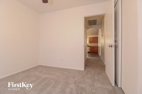 an empty bedroom with a hallway to the kitchen and a door to the bathroom