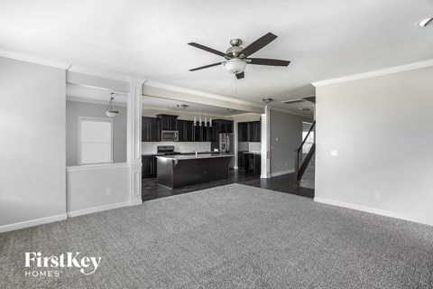 A spacious living room with a grey carpet and a ceiling fan.