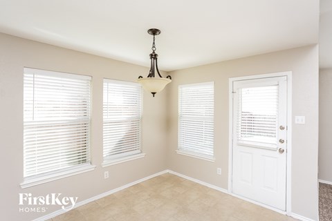 A room with a chandelier, two windows with blinds, and a door.