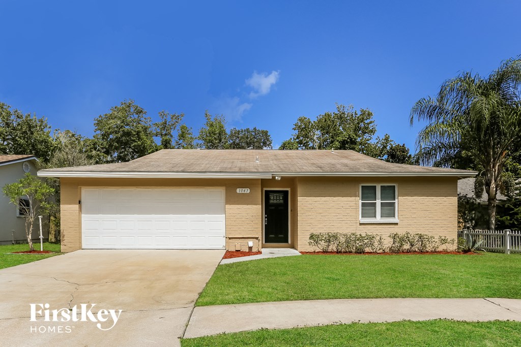 a small tan house with a driveway and a lawn