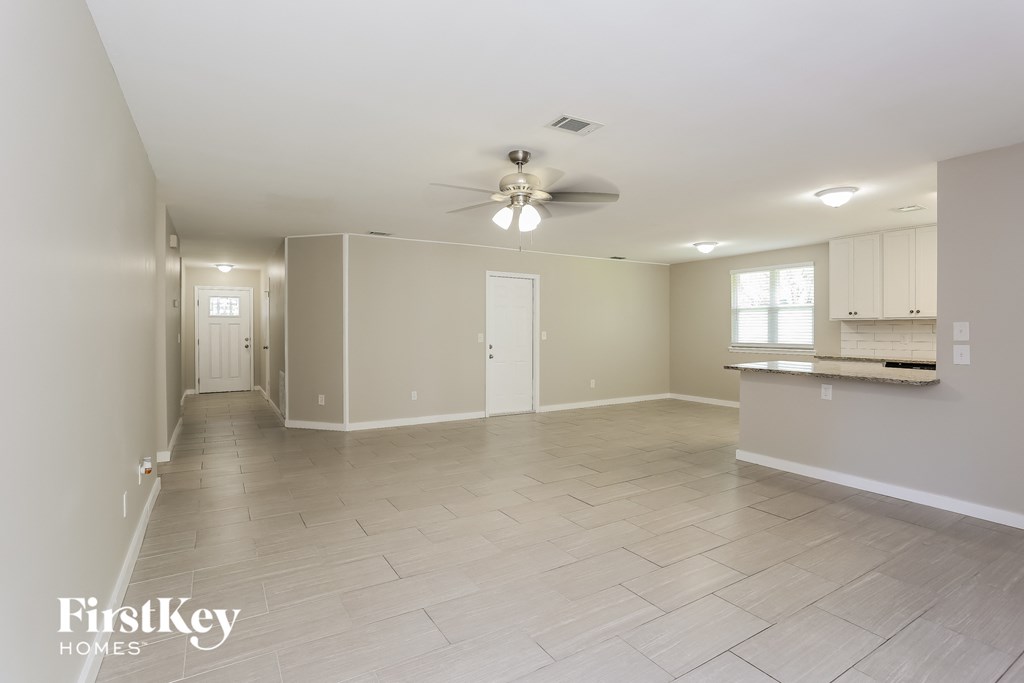 an empty living room with a ceiling fan and a kitchen