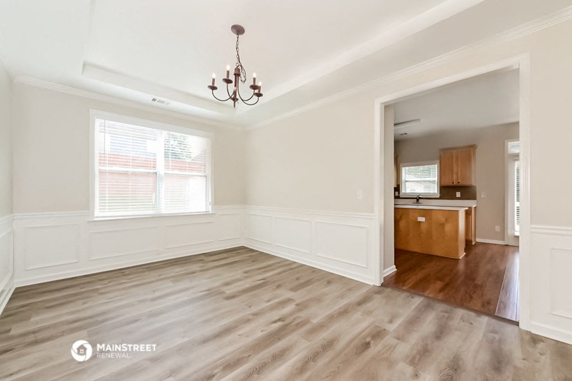 an empty living room with a kitchen in the background and a chandelier