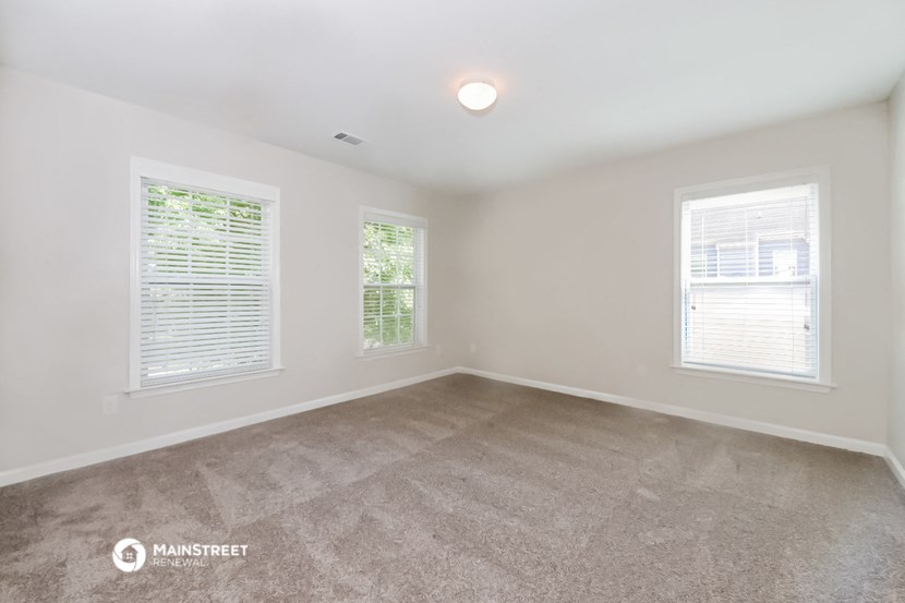 the spacious living room with carpeting and three windows