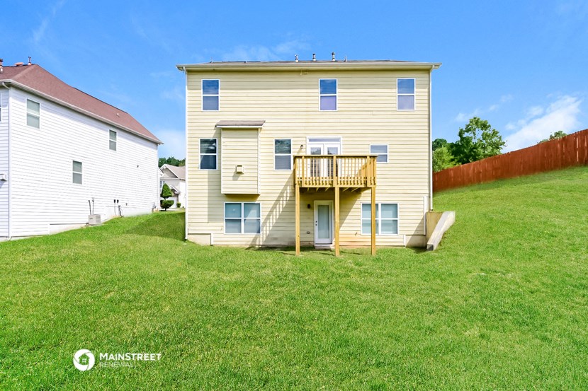 the back of a yellow house with a wooden deck on a lawn