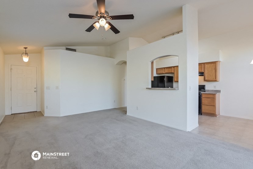 an empty living room with a ceiling fan and a kitchen