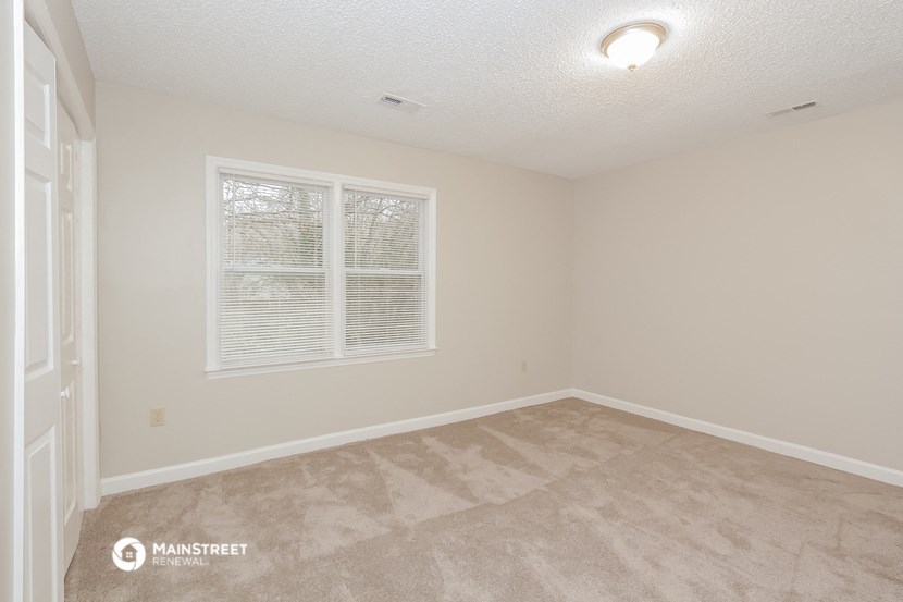 the spacious living room of a manufactured home with beige carpet and a window