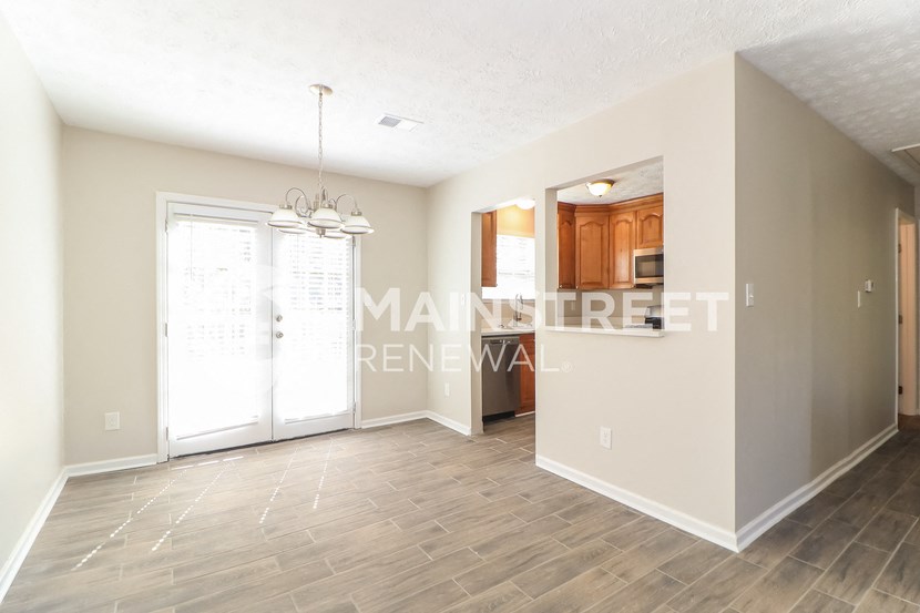 an empty living room with a door to the kitchen and a window