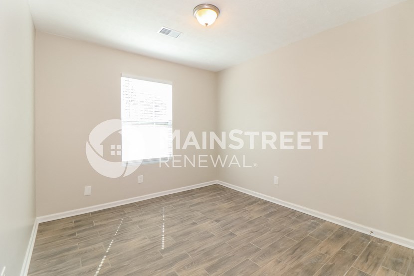 a bedroom with a hardwood floor and white walls and a window