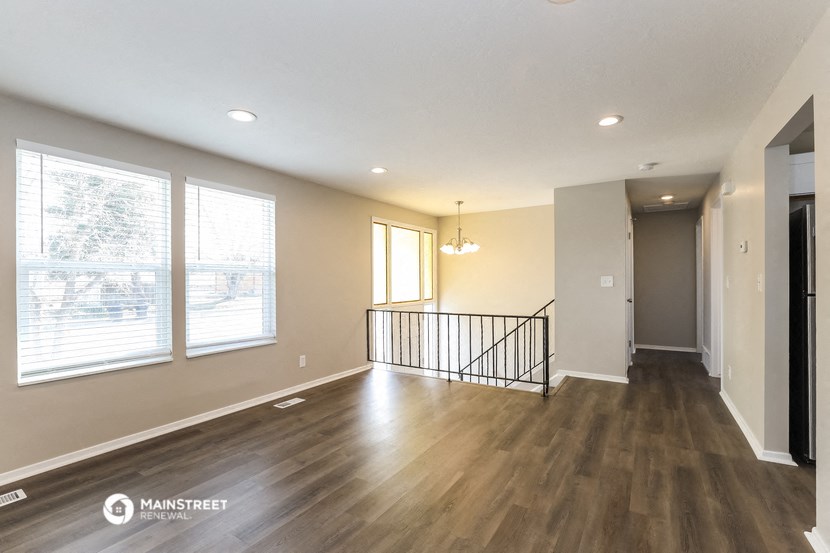 the living room and dining room of a house with wood flooring and large windows