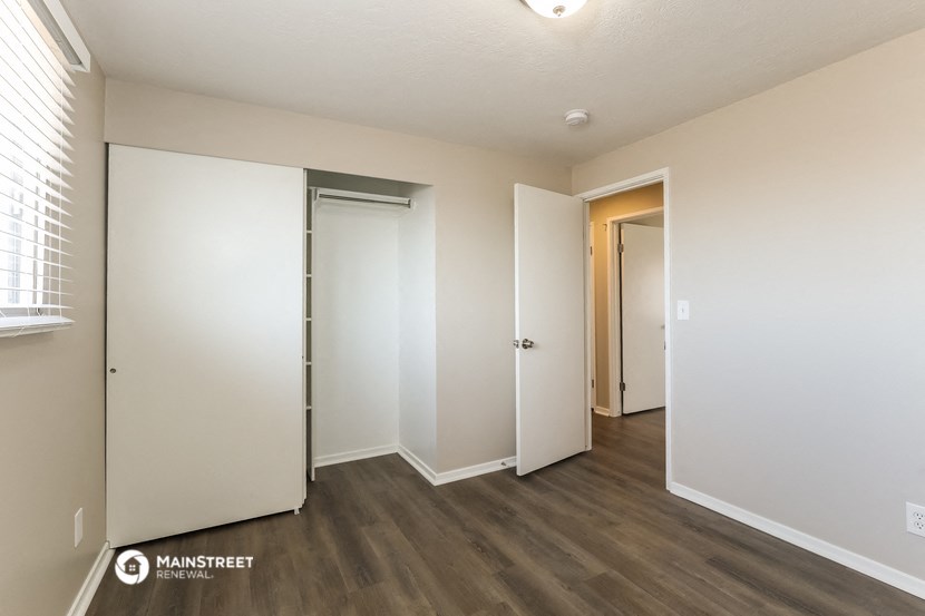 a bedroom with white walls and wood flooring and a closet