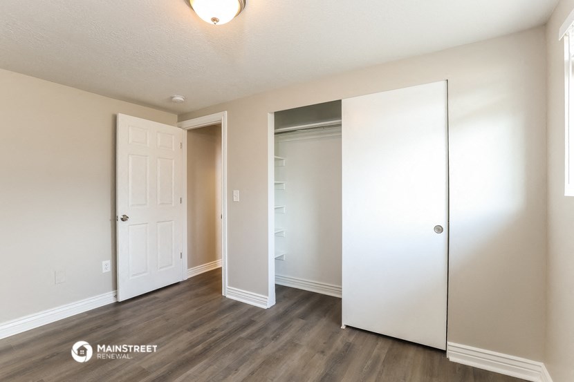 the living room of an apartment with white walls and wood flooring
