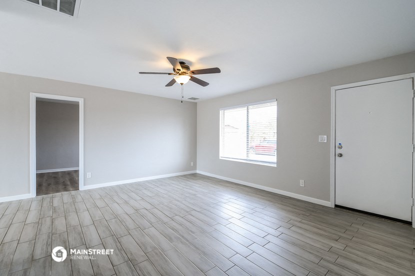 the spacious living room with wood floors and a ceiling fan