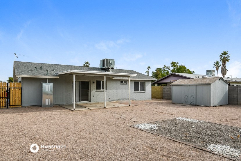 a small gray house with a dirt yard and a garage
