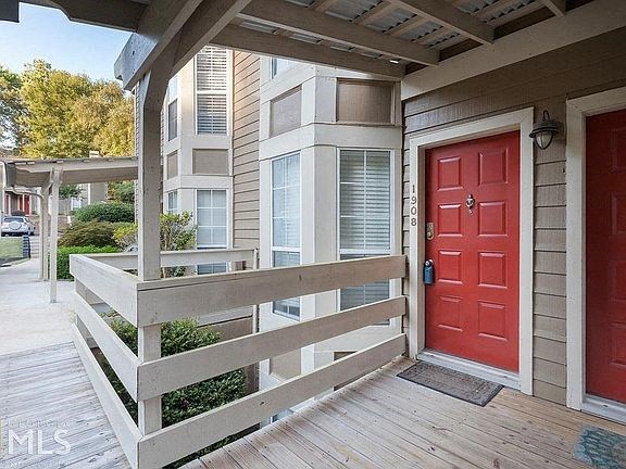 A red door is on the right side of a wooden porch.