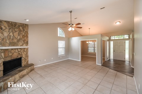 A spacious living room with a stone fireplace and a ceiling fan.