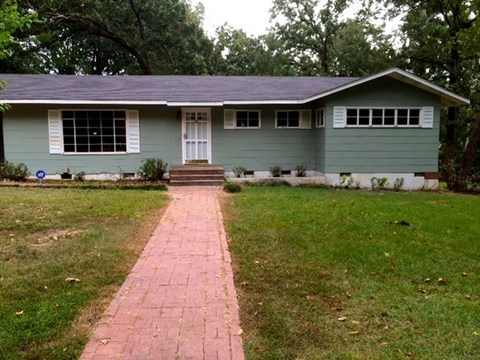 A green house with a brick pathway leading to the front door.