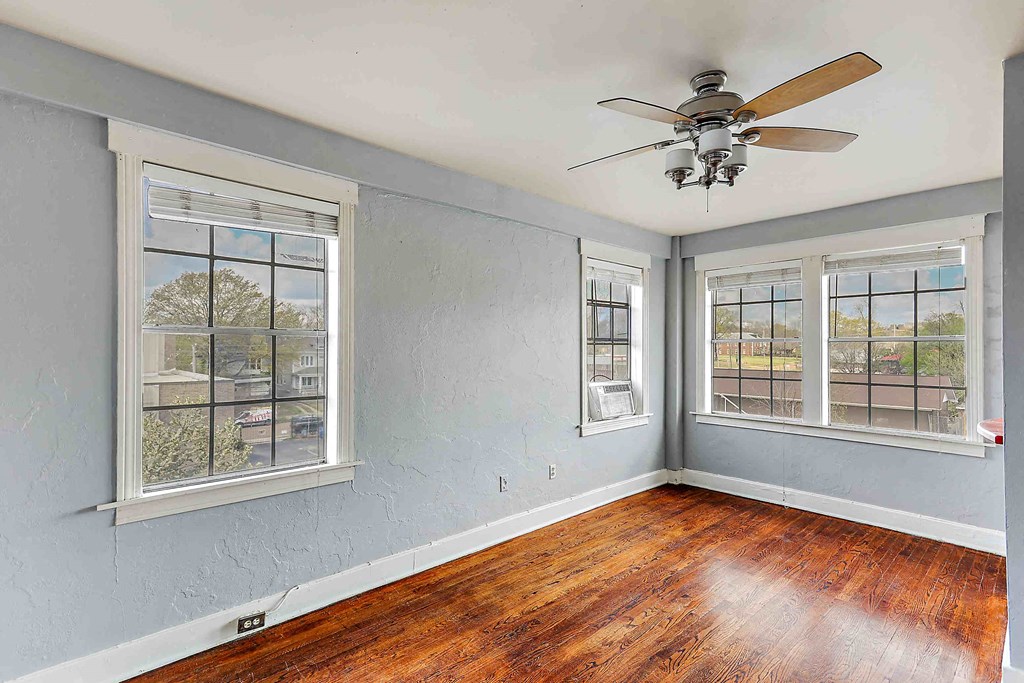 an empty living room with a ceiling fan and three windows