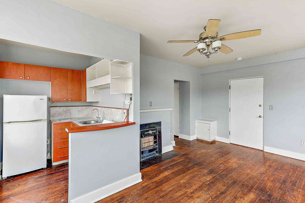 an empty living room with a kitchen and a ceiling fan