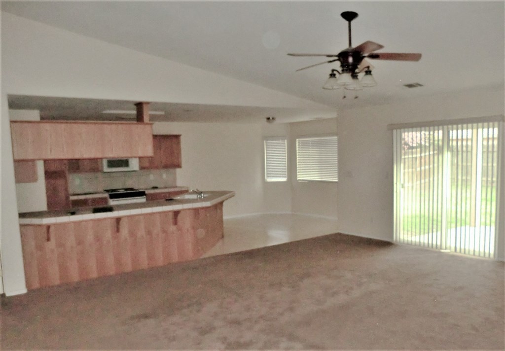 an empty living room with a kitchen and a ceiling fan
