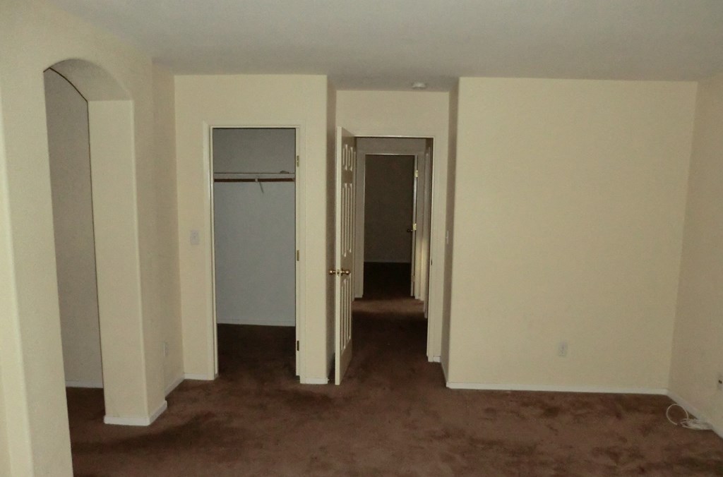an empty room with white walls and a hallway with closets and doors