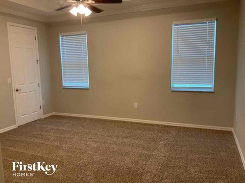 A room with a carpeted floor, a ceiling fan, and two windows with blinds.