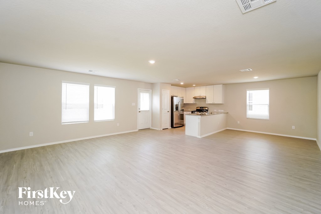 A spacious empty room with wooden flooring and a kitchen area in the background.