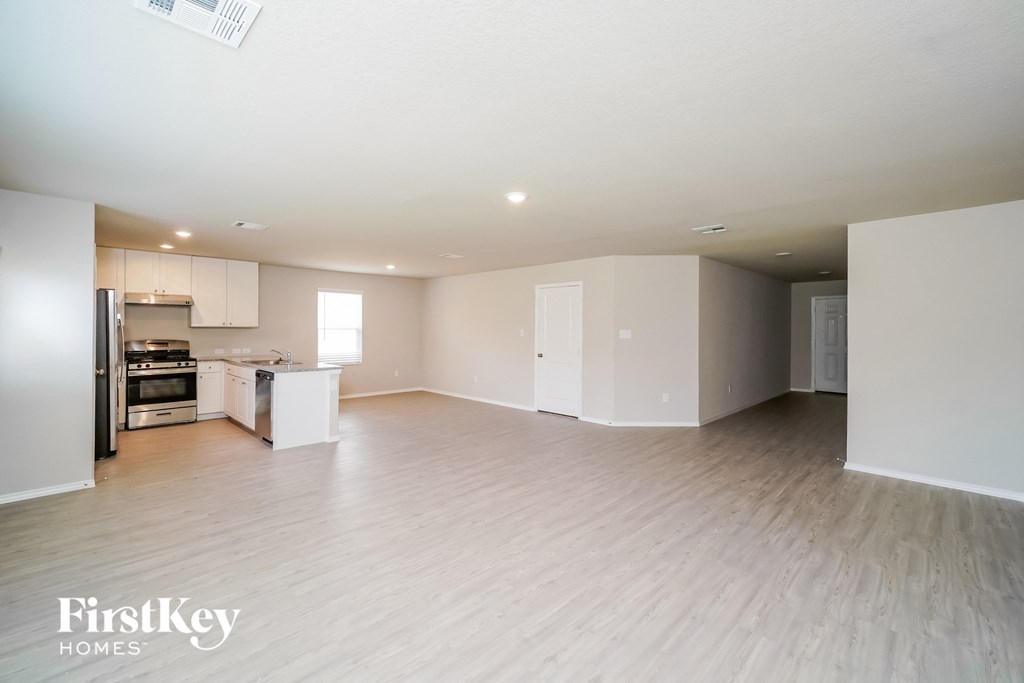 A spacious empty room with wooden flooring and white walls.