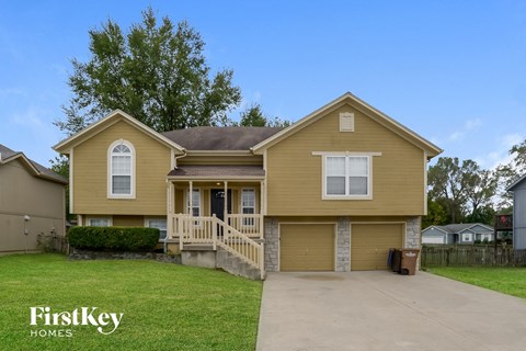 a yellow house with a driveway and a lawn