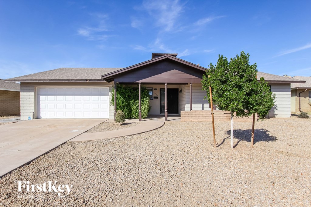 A house with a gravel driveway and a tree in front of it.