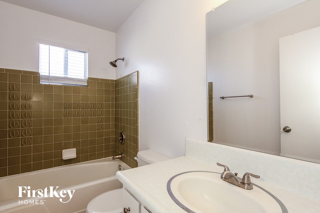 A bathroom with a white tub and brown tiles.