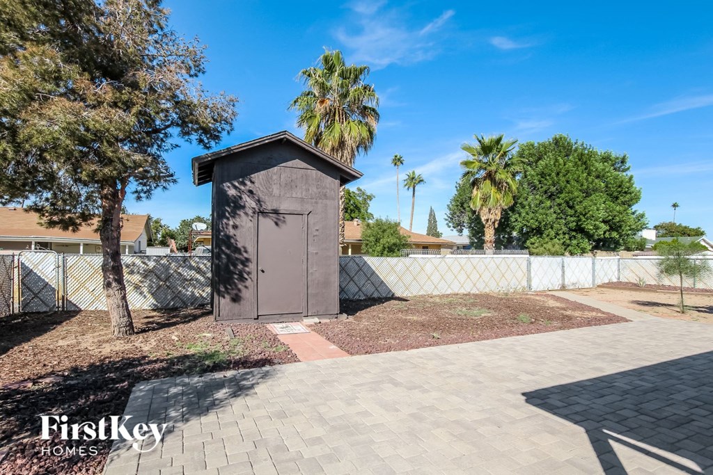 A small building with a brown door is surrounded by a white fence and palm trees.