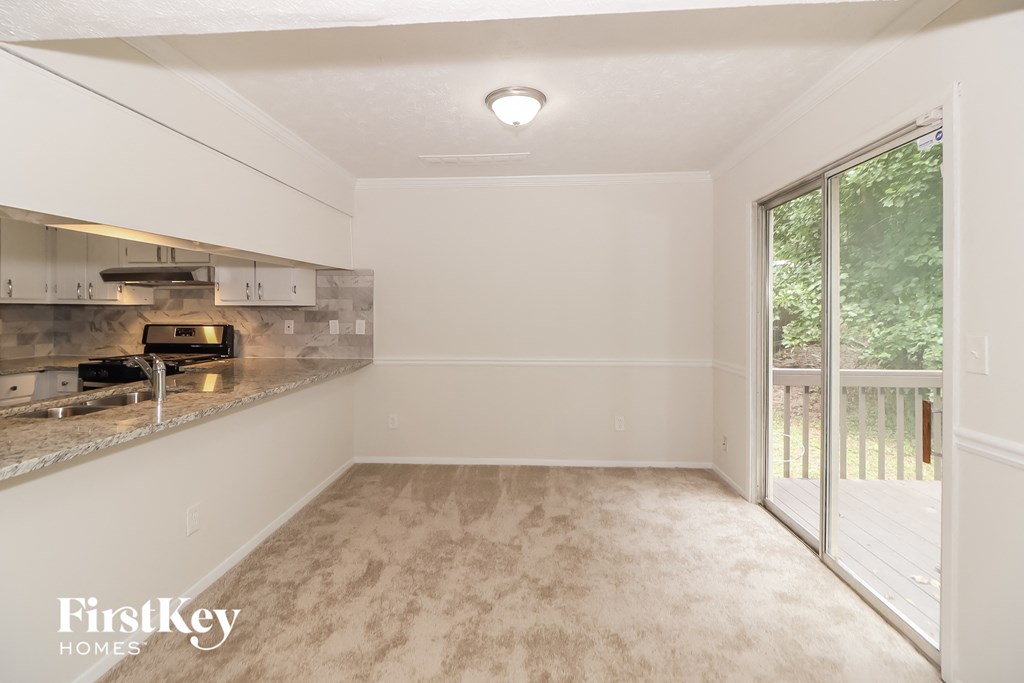 A well-lit, empty room with a kitchen area to the left and a sliding glass door leading to a balcony.