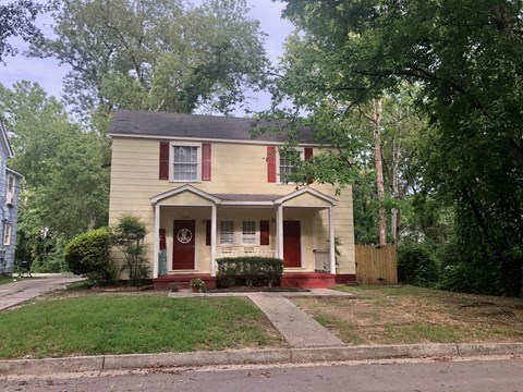 a small yellow house with red shutters and a lawn